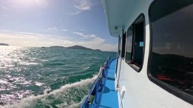 Phuket, Tayland yakınlarındaki berrak sularda sakin bir tekne yolculuğu. Parlak güneş ışığı, nazik dalgalar ve uzak adalar barışçıl bir atmosfer yaratır.