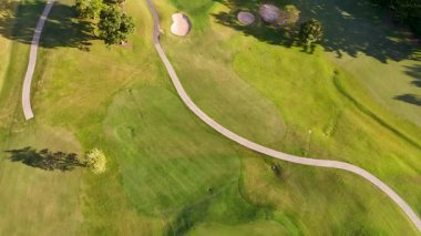 İnsansız hava aracı görüntüleri canlı yeşillikler, kum sığınakları ve parlak güneş ışığı altındaki dolambaçlı yollar içeren yemyeşil bir golf sahası yakalıyor.