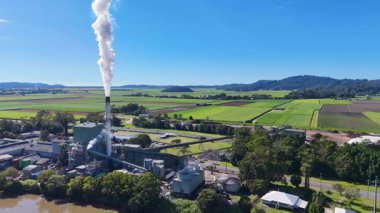 Hava görüntüleri, açık mavi gökyüzünün altında geniş yeşil alanlar arasında buhar yayan bir şeker kamışı fabrikasını yakalıyor.
