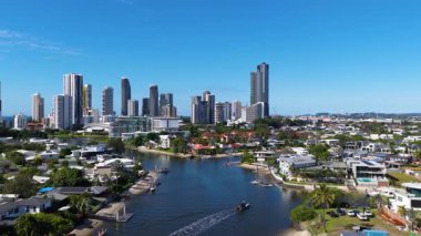İnsansız hava aracı görüntüleri, açık mavi gökyüzünün altında Altın Sahil 'in ufuk çizgisini ve su yollarını yakalıyor. Şehir mimarisi ve doğal güzellikleri gözler önüne seriyor.