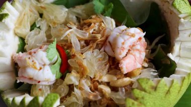 İçinde karides, bitki ve baharatlar bulunan canlı bir Tayland pomelo salatası, güzel oyulmuş bir pomelo kasesinde sunuluyor.