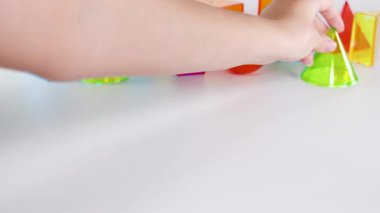 Eller, beyaz bir yüzeyde canlı üç boyutlu geometrik şekilleri manipüle eder, renkli bir ortamda hareket ve etkileşim gösterir