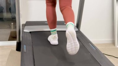 Tozluklu bir kadın, iyi aydınlatılmış bir spor salonundaki koşu bandında koşuyor, spor ve sağlığa odaklanıyor.