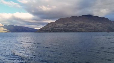 Dağları ve dinamik bulutları olan sakin Wakatipu Gölü. Yumuşak ışık dingin ve dramatik atmosferi güçlendirir.
