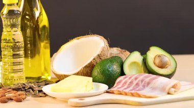 Avokado, hindistan cevizi ve zeytinyağı gibi çeşitli sağlıklı yağ ve yağlar, yumuşak ışıklandırmalı ahşap bir masa üzerine dizilmiştir.