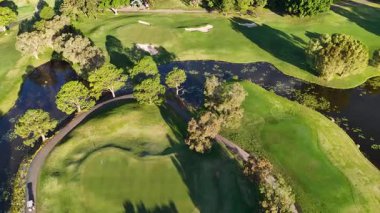 İnsansız hava aracı görüntüleri, parlak güneş ışığı altında golf sahaları, sığınaklar ve su tehlikeleriyle dolu yemyeşil bir golf sahası yakalıyor.