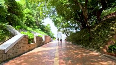 Ağaçlarla kaplı bir park yolunda yürüyen insanlar.