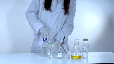 Bir bilim adamı, laboratuvarda kimyasalları kontrollü ışıklandırma ve hassas hareketlerle karıştırarak potasyum karbonat deneyi yürütüyor.