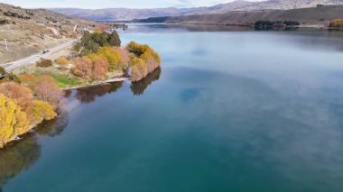 Drone görüntüleri Dunstan Gölü 'nün dingin sularını ve Cromwell, Yeni Zelanda' daki canlı sonbahar yapraklarını yumuşak doğal ışık altında yakar.