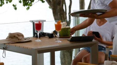 Bir sunucu, Phuket, Tayland sahilindeki bir masaya gün ışığında canlı meyve suyu sunar.