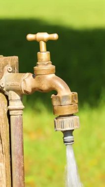 Bir el, bir çiftlikteki pirinç musluğu kapatır ve su akışını durdurur. Parlak gün ışığı açık hava ayarlarını vurgular