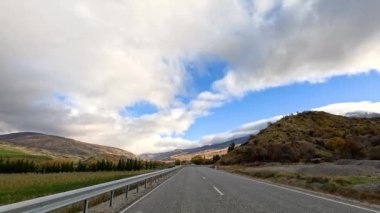Wanaka 'nın resimli yollarında 45 saniyelik bir sürüş, dinamik bulut oluşumları ve açık mavi gökyüzü altında canlı sonbahar renkleri sergiliyor.