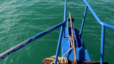 Tayland, Phuket 'teki zümrüt sularında bir balıkçı teknesi süzülüyor. Parlak güneş ışığı parlak mavi ve yeşil renkleri yükseltir.