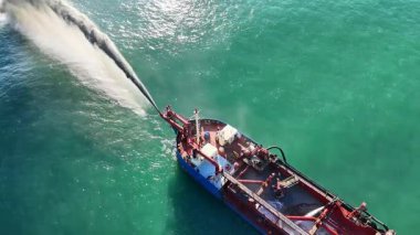 Okyanusa kum pompalayan bir geminin hava görüntüsü, açık gökyüzü altında plaj restorasyonunu arttırıyor.