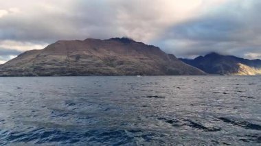 Queenstown, Yeni Zelanda 'daki Wakatipu Gölü' nün sakin manzaraları, dinamik bulut örtüsü altında dağlar ve yumuşak ışıklandırma.