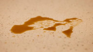 Bir el, sıcak ışık altında benekli bir tezgahın üzerine dökülen kahveyi temizlemek için mavi bir bez kullanır.