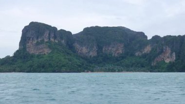 Krabi 'nin çarpıcı kireçtaşı uçurumlarını ve bulutlu gökyüzünün altında yemyeşil çimenliklerini gösteren sakin bir tekne yolculuğu.