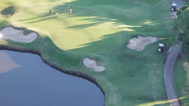 İnsansız hava aracı, altın saat boyunca yemyeşil bir çayırda altın rengi bir golf sahasında golfçüleri yakalıyor.