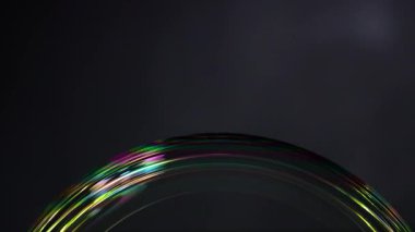 Bir sabun köpüğü, karanlık bir arkaplan, ışık etkileşimi ve yüzey gerilimi karşısında canlı renk yansımaları gösterir