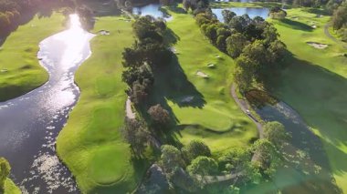 İnsansız hava aracı, altın saat boyunca yemyeşil ve su özellikleriyle sakin golf sahası yakalar.