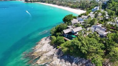 Drone, Phuket 'in sahil şeridinin çarpıcı hava görüntülerini yakalıyor, turkuaz sular, yemyeşil alanlar ve parlak güneş ışığı altında lüks villalar sergiliyor.