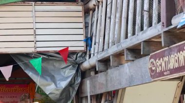 Khlong Lat Mayom Dalgalanan Market 'teki ahşap yapının detaylı bir görüntüsü, canlı bayraklar ve kırsal bir işaret.