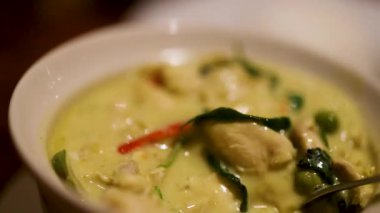 Tayland yeşil körisinin karıştırıldığı, canlı malzemelerin ve zengin dokuların sıcak, davetkar bir şekilde sergilendiği yakın çekim videosu.