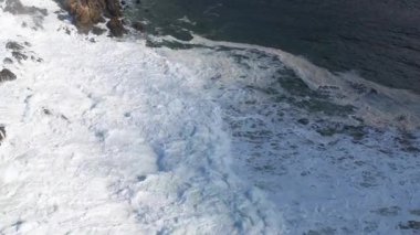 Hava görüntülerinde Byron Bay 'in kayalık sahil şeridine çarpan dalgalar görülüyor. Doğal gün ışığı altında, dinamik okyanus hareketi ve engebeli arazi gösteriliyor.