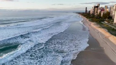İnsansız hava aracı gündoğumunda Gold Coast 'un dalgalarını ve sahil şeridini yakalıyor, sakin plajı ve kentsel ufuk çizgisini vurguluyor