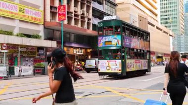 İnsanlar çift katlı tramvayın yanında karşıdan karşıya geçiyor.