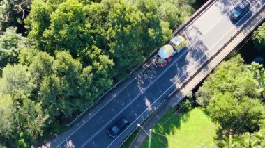 Hava görüntüleri bir çimento kamyonunu parlak güneş ışığı altında yemyeşil bir orman yolundan geçerken yakalıyor.