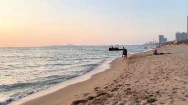 İnsanlar gün batımında sahilde yürüyorlar.