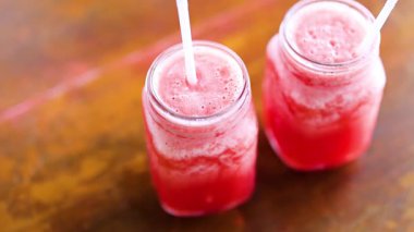 Bir el, ahşap bir masada karpuz suyunu karıştırıyor ve canlandırıcı bir içecek hazırlıyor.