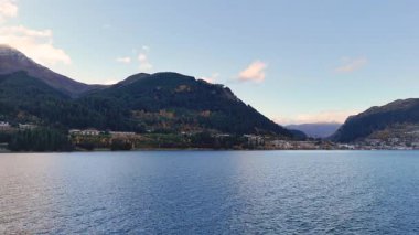 Queenstown, Yeni Zelanda 'daki dağlarla çevrili sakin bir göl manzarası. Gün ışığında sakin sularda ve berrak gökyüzünde yakalandılar.