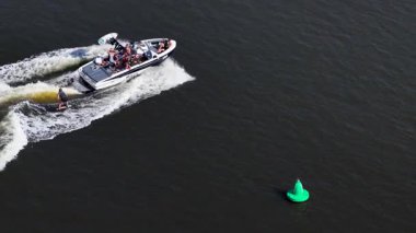 İnsansız hava aracı, yolculuğun tadını çıkaran yolcularla birlikte sularda yüzen bir tekne yakalıyor. Parlak gün ışığı dinamik sahneyi güçlendirir