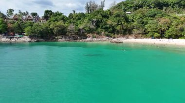 İnsansız hava aracı görüntülerinde Phuket, Tayland 'da sakin bir sahil görüntüsü var. Turkuaz sular, uzun kuyruklu botlar ve parlak gün ışığında yemyeşil alanlar sergileniyor.