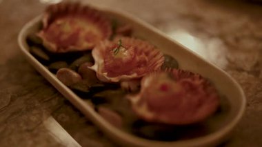 Izgara deniz tarakları dekoratif bir tabakta sunuluyor, sıcak ortam ışıklarıyla çekiliyor ve mutfak sanatına odaklanıyor.