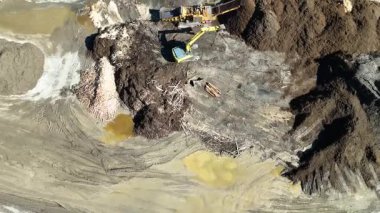 İnsansız hava aracı görüntülerinde güpegündüz kirli bir arazide gübre yığınları taşıyan bir kazıcı görülüyor.