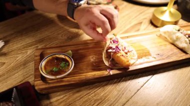 Sıcacık bir Meksika restoranında tako hazırlayan ve tadını çıkaran bir insan, canlı malzemeleri ve davetkar atmosferi ön plana çıkarıyor.