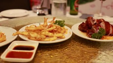 Döner bir masada Çin yemekleri, soslar ve yemek çubukları sıcak ışıklandırmalı bir restoran ortamında sergilenir.