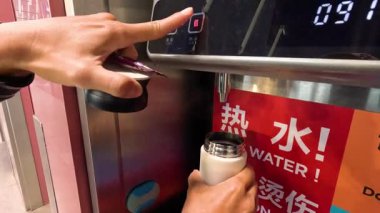 Seyahat kupasını halka açık sıcak su dağıtıcısından dolduran kişi