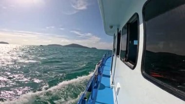 Phuket, Tayland yakınlarındaki berrak sularda sakin bir tekne yolculuğu. Parlak güneş ışığı, nazik dalgalar ve uzak adalar barışçıl bir atmosfer yaratır.
