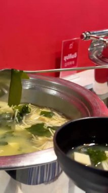 Bangkok 'ta Kore barbeküsünde miso çorbasını bir kaseye koyan bir adam. Parlak ışıklandırma çorbanın içeriğini vurgular