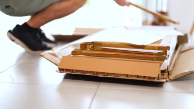 Bir insan karton bir kutuyu fayansla döşenmiş bir zemin üzerinde açar ve iyi aydınlatılmış bir odadaki içeriği ortaya çıkarır.