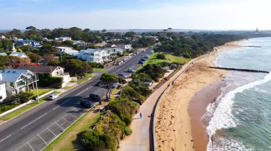 Hava görüntüleri, sakin sahil çevresini aydınlatarak, Point Lonsdale sahilinin yanındaki açık gökyüzünün altında manzaralı bir kıyı yolu yakalıyor.