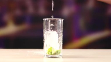 Buzlu ve limonlu bardağa sıvı döküldüğünü gösteren bir sahne bulanık bir arka plana ayarlanmış.