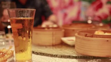 Dim Sum, renkli tabaklar ve masada bir bardak birayla hayat dolu bir restoran sahnesi.