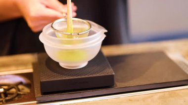 El çırpışı bir kasede belli bir ölçekte, geleneksel çay yapma tekniklerini belirgin hareketlerle ve canlı yeşil renklerle vurguluyor.