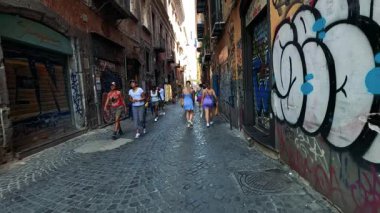 Turistler duvar yazısıyla kaplı bir sokakta yürürler.