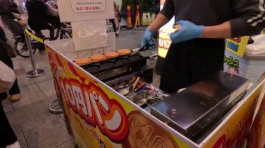 Tedarikçi işlek sokak tezgahında sosis ızgarası yapıyor.